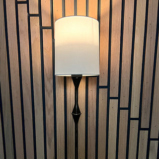 Illuminated battery wall sconce with white shade casting warm glow on modern geometric wood wall