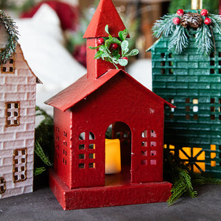 Red metal church lantern with candlelight glow and holly wreath, part of a festive Christmas village decoration set