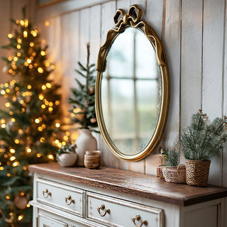Antique gold oval mirror with decorative bow accent hanging on white shiplap wall above farmhouse console table with Christmas decor