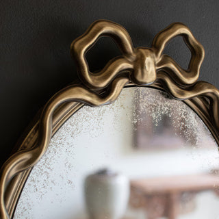 Close-up detail of decorative metal bow accent on antique gold oval mirror frame showing craftsmanship