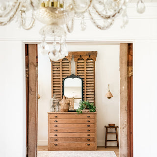 Elegant arched mirror with decorative crest styled on farmhouse console table with greenery