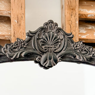 Detailed view of intricate scrollwork and floral baroque crest on black distressed mirror frame