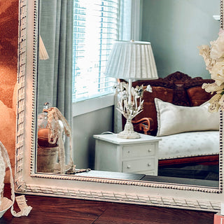 White farmhouse mirror reflecting cozy bedroom decor