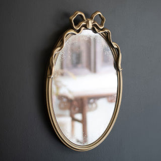 Antique gold oval mirror with bow detail mounted on dark wall showing full mirror reflection and vintage character