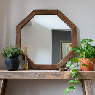 Octagon wood-framed mirror resting on a rustic wooden shelf with potted plants and reed diffuser for interior styling