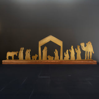 Full brass nativity scene silhouette on wooden base against dark backdrop, minimalist Christmas mantel or shelf décor.