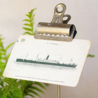  Close-up of antique brass finish metal binder clip holder displaying vintage ship postcard