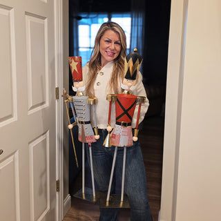 Person holding a pair of tall metal nutcracker figurines with gold and red detailing, showing scale for holiday home decor.