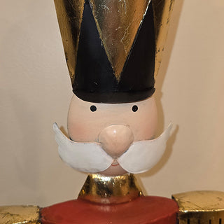 Close-up of nutcracker face with painted mustache, round nose, and tall black hat with gold detailing.