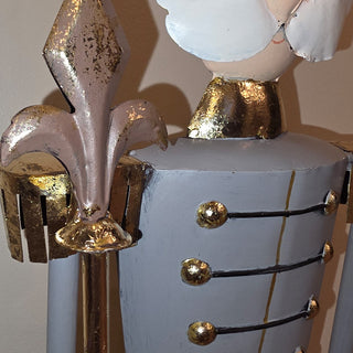 Detailed view of metal nutcracker holding a gold and bronze fleur-de-lis staff with distressed metallic finish.