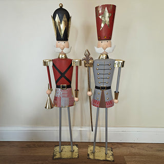 Two tall metal nutcracker decorations standing side-by-side on distressed gold bases, featuring red, grey, and gold holiday detailing.