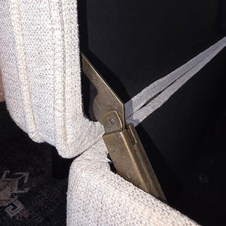 Close-up detail of gold metal hinge mechanism on cream boucle storage ottoman showing quality hardware