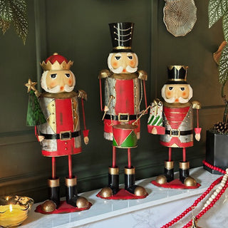 Set of three painted metal nutcracker Christmas figurines in red and gold outfits, displayed on a mantel for holiday home décor