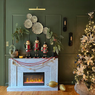 Christmas mantel décor featuring nutcracker figurines, greenery, garlands, and a lit Christmas tree beside a fireplace
