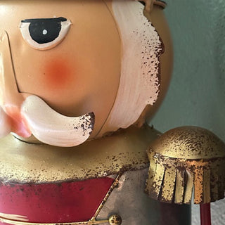 Close-up of painted metal nutcracker figurine with vintage finish, showing detailed face and gold shoulder accents