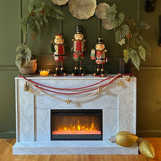 Nutcracker figurines displayed on a decorated Christmas mantel with garlands and candles above a glowing fireplace