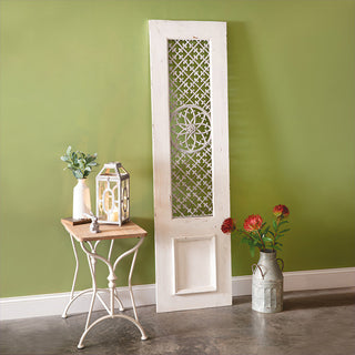 Vintage-style white distressed door panel with metal lattice and floral detail leaning beside small accent table