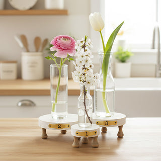 Three numbered white wood pedestal risers displaying bud vases with spring flowers on kitchen counter