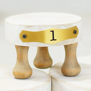 Close-up of small numbered pedestal riser with gold plate showing number 1 and turned wooden legs