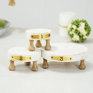 Three numbered farmhouse pedestal risers arranged on table with greenery and candle in background