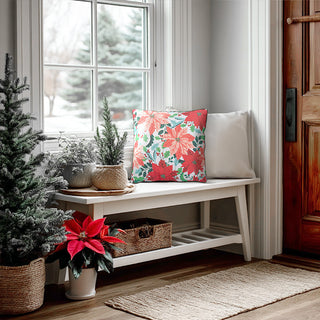 Poinsettia floral Christmas pillow on white entryway bench near window with holiday decor and mini Christmas trees