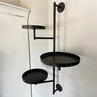 Three-tier black iron wall-mounted plant stand with circular trays displayed empty against a white wall.