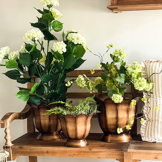 Decorative bronze planters with hydrangeas on wooden bench
