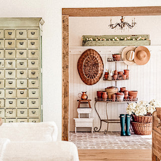Nestled corner of a room with rustic decor elements including a wooden shelf, a plant stand with pots, a vintage cabinet, and a chandelier.