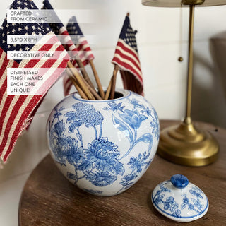 Decorative Chinoiserie Ginger Jar with blue floral patterns on a wooden surface, with American flags and a gold lamp in the background.