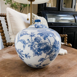 Blue and white floral-patterned Chinoiserie Ginger Jar on a wooden table with a lamp and decorative items in the background.