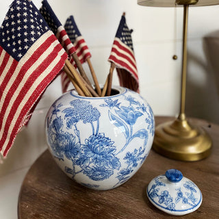 Decorative blue and white floral-patterned Chinoiserie Ginger Jar with American flags on a wooden surface.