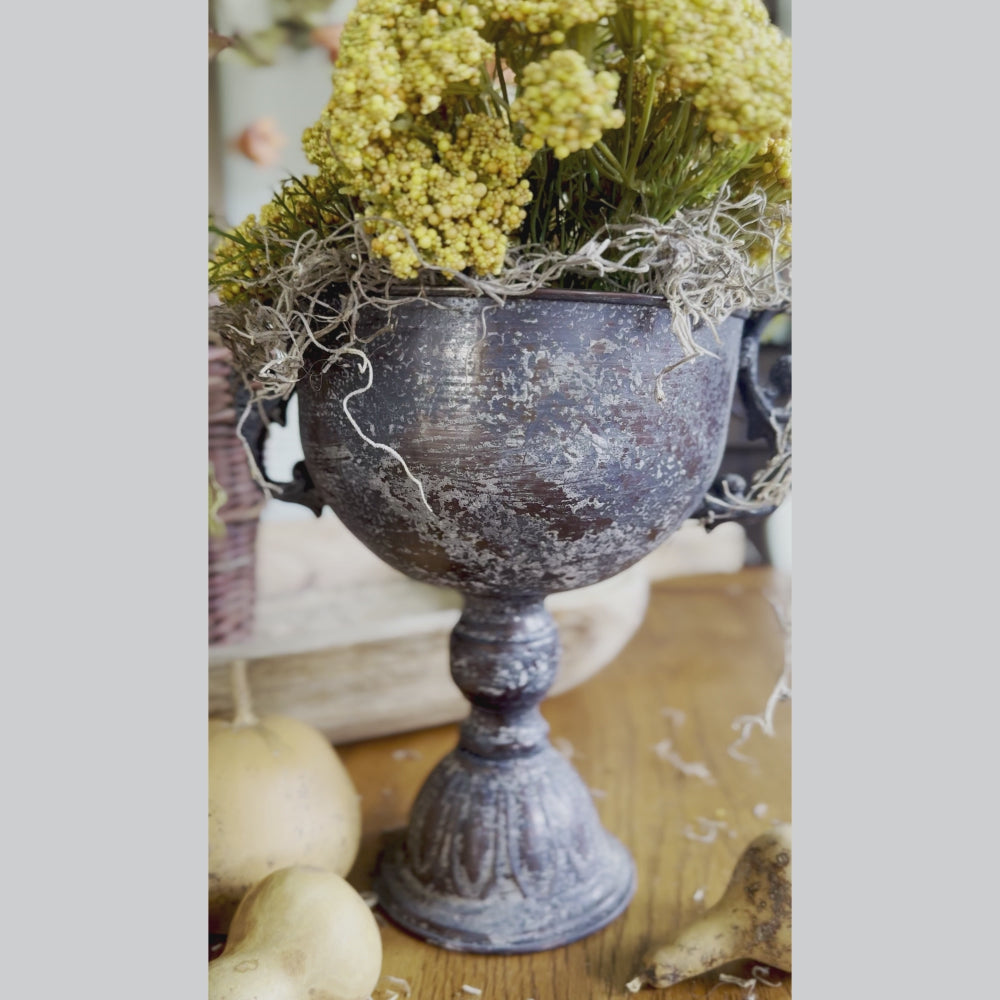 Decorative black urn with dried flowers on a wooden surface