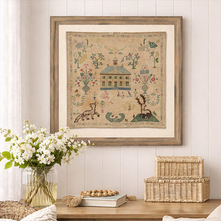 Vintage colonial house embroidered sampler wall art in weathered wood frame displayed above console table with white flowers