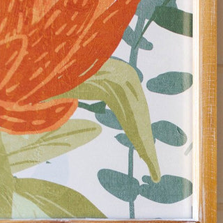 Close-up of vibrant orange protea bloom and green botanical leaves behind glass on framed wall art