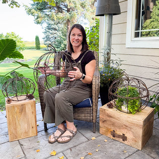 Woman sitting on outdoor patio holding decorative metal pumpkin-shaped wire sculpture
