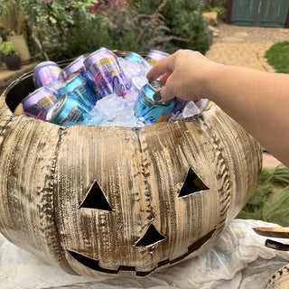 Hand grabbing soda can from distressed metal pumpkin ice bucket filled with drinks and ice