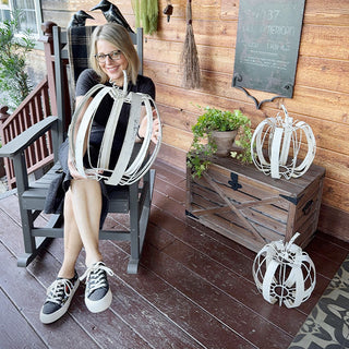 Woman sitting on a rocking chair holding large distressed white metal pumpkin decor on farmhouse porch