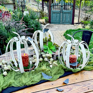 Rustic fall table centerpiece with set of three white metal pumpkins, candles, greenery, and decorative accents