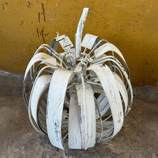 Distressed white metal pumpkin sculpture with rustic farmhouse finish against yellow wall background