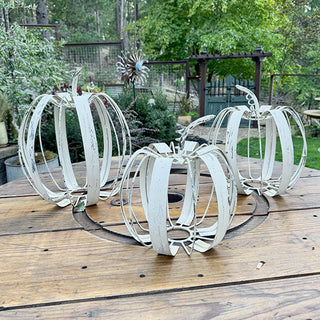 Set of three farmhouse white metal pumpkin decorations styled on outdoor wooden table for fall decor