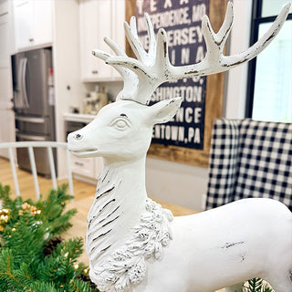 Close-up of standing white distressed resin deer statue with carved wreath detail around neck, styled in modern farmhouse kitchen