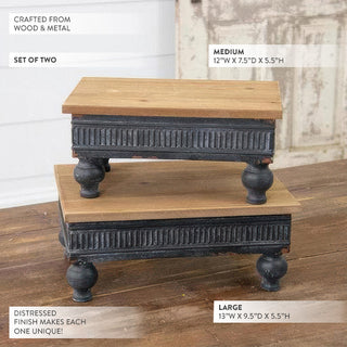 Set of two wood risers showing medium and large sizes with distressed black metal ribbed base and turned feet
