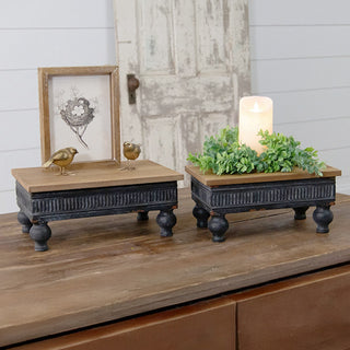 Two farmhouse risers styled on console table with framed artwork, bird figurine, greenery, and pillar candle