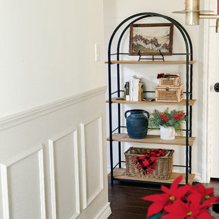Decorative arched wood and metal bookshelf in hallway corner, styled with seasonal home décor and natural accents