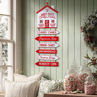 North Pole Candy Parlor metal directional sign with red and white arrows hanging on sage green wall with holiday wreath and candy jars