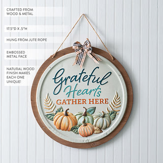 Close-up of rustic wood and metal wall décor sign with embossed pumpkins and plaid bow, reading 'Grateful Hearts Gather Here