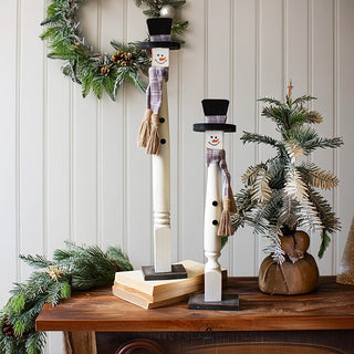 Farmhouse wooden snowman set with black top hats and plaid scarves displayed on rustic wood table with Christmas greenery