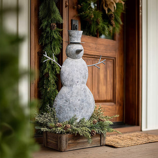 Distressed white metal snowman with galvanized bucket hat on wooden porch with evergreen garland and Christmas decorations