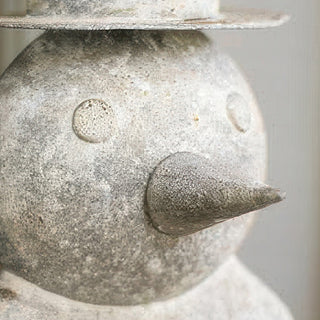 Close-up detail of distressed white metal snowman face showing carved smile and textured weathered finish