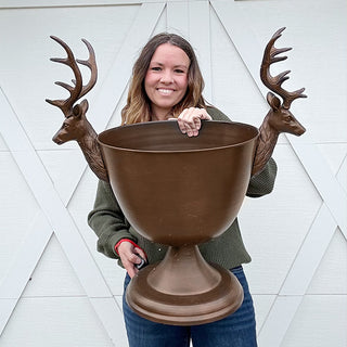 Woman holding oversized bronze stag pedestal bowl with sculpted deer head handles, showcasing large holiday centerpiece decor